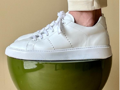 Premium white National Standard sneaker on a green stool, ethical Portuguese craftsmanship